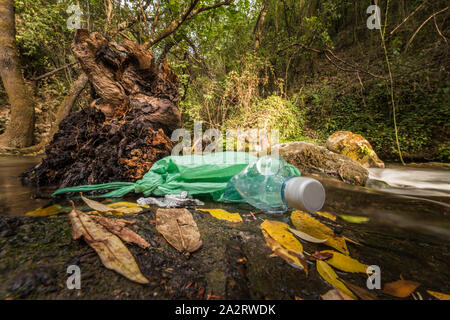 Garbage in un abbandonato il sacchetto in plastica sulla sponda di un fiume di acqua pulita. Concetti di danno ambientale e riciclaggio dei contenitori di plastica. Foto Stock