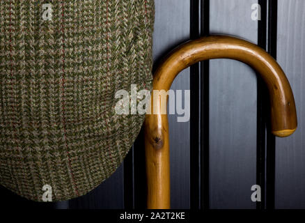 Bastone da passeggio e tweed cap appeso su nero antina Foto Stock