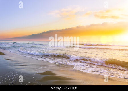 Onde sul mare prima del tramonto, il sole splende tra le nuvole Foto Stock
