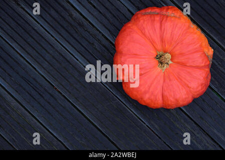 Una grande zucca arancione si trova su nero di tavole di legno come sfondo con posto per il testo in autunno su Halloween Foto Stock