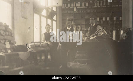 Fotografia digitale - Vista interna e il personale di PL & B fabbrica ombrelli, Melbourne, 1913, tre uomini e un ragazzo a lavorare in una fabbrica di ombrello. Due uomini sono in piedi dietro un contatore e l'uomo a sinistra è appoggiata su una pila di colli. Questa fotografia mostra gli interni e i lavoratori di P. L..& B. Ombrello Fabbrica, Melbourne, 1913. La sua famiglia si ricorda che questo è stato Walter Burke del primo posto di lavoro quando era un giovane uomo Foto Stock