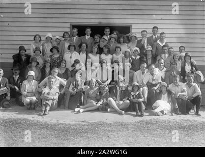 Negativo di vetro - Ritratto di gruppo, circa 1920S, bianco e nero, metà piastra negativa con un gruppo di uomini, donne e bambini che pongono al di fuori, nella parte anteriore di un edificio in legno Foto Stock