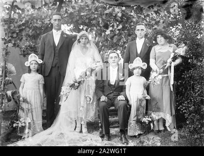 Negativo di vetro - Ritratto di gruppo della festa di nozze, circa 1920s, una in bianco e nero, metà piastra negativa con un ritratto di nozze circa 1920s. Il govern è seduto mentre la moglie, con bouquet ampio e lungo velo nuziale, damigella, due groomsmen e due ragazze di fiori stand intorno a lui. Il gruppo è circondato dalla vegetazione Foto Stock