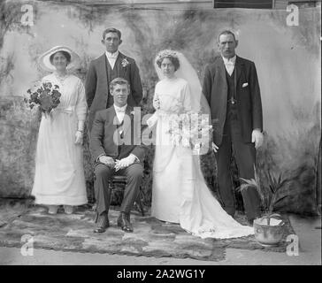 Negativo di vetro - Gruppo Studio ritratto della festa di nozze, circa 1910s, una in bianco e nero, metà piastra negativa di copia con un ritratto in studio di una festa di nozze, circa 1910s. Il govern è seduto mentre la moglie, con bouquet ampio e lungo velo nuziale, damigella con bouquet e due groomsmen stand intorno a lui Foto Stock