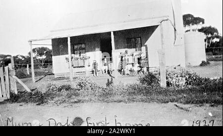 Negativo - Chinkapook, Victoria, 1927, una famiglia sulla veranda della loro ferro corrugato home. Essi hanno gli inizi di un giardino frontale, comprese le piante in vaso lungo la veranda. Il cortile anteriore è recintata con rete metallica e vi è un serbatoio di acqua sul retro della casa Foto Stock