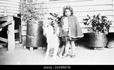 Negativo - Chinkapook, Victoria, 1930, un bambino con un collie cane. Il bambino è che indossa un capo con cappuccio. C'è un gatto sulla destra. In fondo è un serbatoio di acqua e due fusti contenenti piante Foto Stock