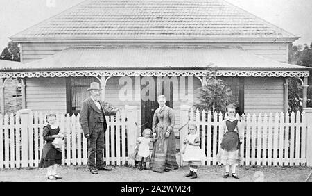 Negativo - Famiglia di fronte a una casa, Clunes, Victoria, circa 1890, un uomo, donna e quattro bambini piccoli in piedi di fronte a una casa. La casa è un legno di Victorian House con Picket Fence, trine ferro battuto sulla veranda e tetto di ardesia Foto Stock