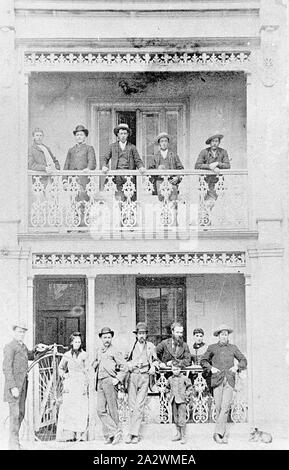Negativo - Gruppo sulla terrazza balcone della casa con Penny Farthing bicicletta, Ballarat, Victoria, circa 1885, un gruppo di persone sul balcone e di fronte a due piani casa terrazza. L'uomo a sinistra regge un penny farthing bicicletta Foto Stock