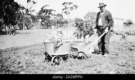 Negativo - i bambini nel carrello Home-Made spinto da uomo, Manangatang, Victoria, circa 1925, un uomo spingendo una fatta in casa carrello. Ci sono due piccoli ragazzi seduti in un cestello di lavaggio sulla parte anteriore del carrello mentre il retro del carrello contiene un vuoto che la scatola di legno Foto Stock