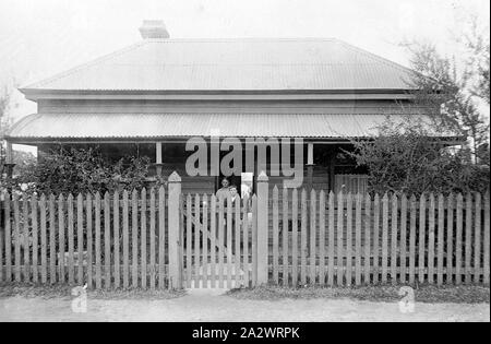 Negativo - Casterton, Victoria, circa 1900, una donna e un ragazzo sulla veranda di una casa. Vi è un Picket Fence in primo piano Foto Stock