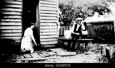 Negativo - La famiglia inverno, Nietta, Tasmania, 1934, una donna Durlie (inverno) è in ginocchio al di fuori di un caseificio. Lei è il lavaggio del pavimento. Un uomo Jack (inverno) è seduta su una panchina accanto al caseificio e poggia il suo gomito su che cosa può essere una zangola Foto Stock