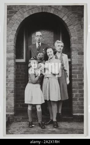 Fotografia - Palmer famiglia al di fuori casa, Iver, Inghilterra, circa 1947, fotografia in bianco e nero di George e Gertrude Palmer e le loro figlie Shirley e Lesley, e il loro cane Robbie, in Inghilterra intorno al 1947. Probabilmente è stato preso a George la sorella in casa Iver, Buckinghamshire da George cognato David Roberts, il giorno prima della partenza per l'Australia. È stato portato in Australia da George Palmer quando egli emigrarono in Australia dall'Inghilterra con sua moglie Foto Stock