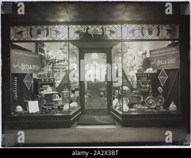 Fotografia - Hecla prodotti in Roses fornitori elettrici, Brunswick, circa 1940, fotografia in bianco e nero del shopfront di rose fornitori elettrici, Sydney Road Brunswick. Esso dispone di prodotti Hecla nella finestra di visualizzazione tra cui riscaldatori [noti poi come gli incendi elettrici], stufe, bollitori e grillers. Numerosi segni dimostrano Hecla slogan come "Alleggerire il peso del giorno " e " mantenere tale aspetto giovanile". Funzioni di immagine un doppio negozio di fronte la finestra di visualizzazione di Hecla Foto Stock