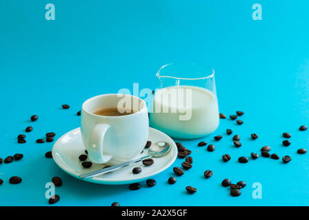 I chicchi di caffè intorno a una tazza di caffè con una brocca o un laboratorio bicchiere pieno di latte Foto Stock