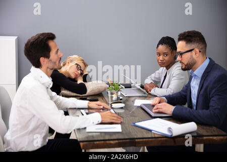 Stanco imprenditrice dormendo mentre seduto sulla scrivania in ufficio con i suoi colleghi Foto Stock