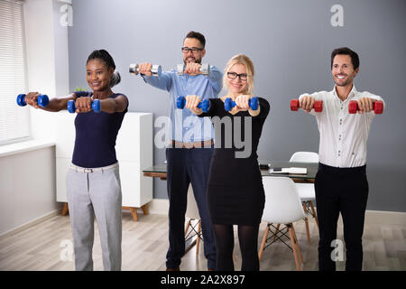 Felice giovani imprenditori in piedi in fila esercizio con manubri in Office Foto Stock