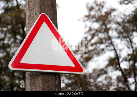 Svuotare un triangolo rosso cartello stradale con non testo e segno su strada e verdi alberi in background Foto Stock