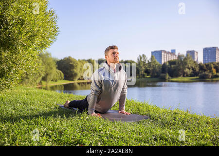 Ispirato uomo fare yoga asana nel parco della città. Centro Fitness all'aperto e di vita il concetto di equilibrio. Foto Stock