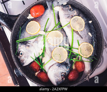 Crudo di pesce orata in padella la cottura con il limone, pomodori e vegetazione. Vista superiore Foto Stock