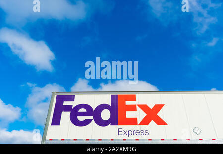 FedEx Express segno sul lato di FedEx Corporation consegna carrello parcheggiato all'aperto sotto il cielo blu con nuvole di luce Foto Stock