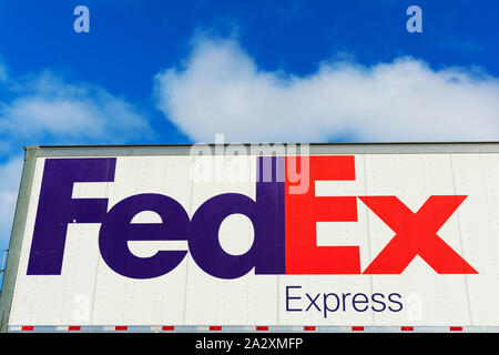 FedEx Express segno sul lato di FedEx Corporation consegna carrello parcheggiato all'aperto sotto il cielo blu con nuvole di luce Foto Stock