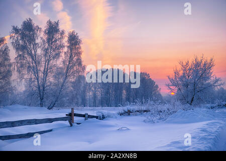 Siberian rurali paesaggio invernale. Alba in campagna. Trave in legno recinto sul primo piano e alberi coperti di brina sullo sfondo Foto Stock