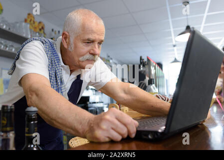 Maschio senior barista guardando al laptop Foto Stock
