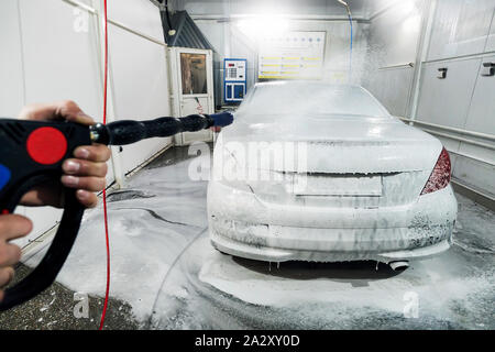 Lavaggio auto con schiuma in auto la stazione di lavaggio. Un uomo di  schiuma spray sulla vettura da un apposito spray. Lavoratore di sesso maschile  lavare la vettura con idropulitrice ad alta
