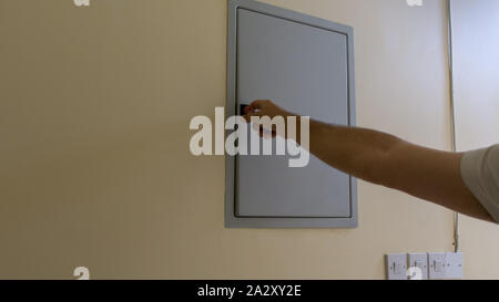 La mano si apre la scatola dei fusibili in una casa residenziale guardando l'interruttori elettrici che fissa la perdita di potenza. Foto Stock