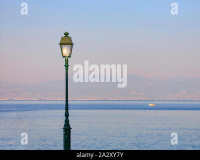 Un lampione è illuminata dai raggi del sole al tramonto con lo sfondo del mare baia. Foto Stock