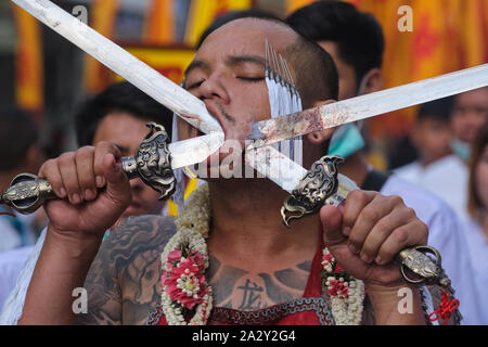 Una processione durante il Festival vegetariano nella città di Phuket, in Thailandia, con un partecipante che mostra una spada trafitto attraverso la guancia Foto Stock