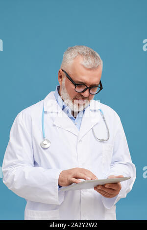 Coppia grave medico in occhiali e in camice bianco con tavoletta digitale nel suo lavoro mentre in piedi su sfondo blu Foto Stock