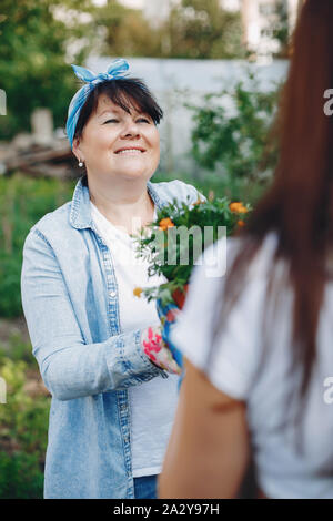 La donna lavora in un giardino. Madre e figlia adulta sono il trapianto di vasi per fiori Foto Stock