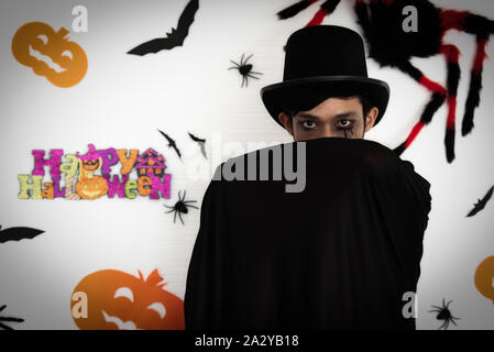 Uomini asiatici per il make-up e abito in Dracula per la festa di Halloween. Egli si alzò e coperto il viso con orrore, ragni, pipistrelli, e zucca sul dietro. Foto Stock