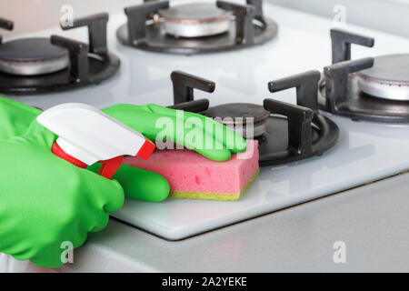 Primo piano della mano nel guanto protettivo tenendo la bottiglia spray e spugna. La pulizia della cucina, fornello a gas. Foto Stock