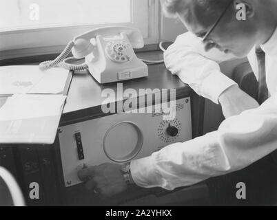 Un hotel guest sta utilizzando la camera di albergo radio e cambia il canale. A destra sul display, egli può inserire il periodo di tempo quando si vuole l'allarme si spengono sul suo servizio di sveglia. 1957 Foto Stock