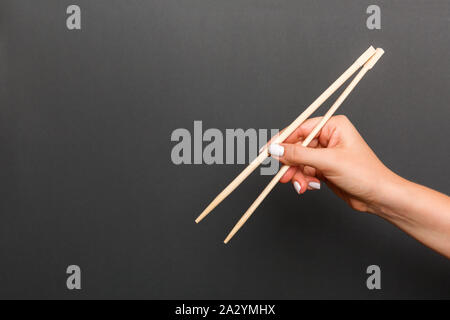 Immagine creativa delle bacchette di legno nelle femmine di mano su sfondo nero. Il giapponese e il cinese del cibo con copia spazio. Foto Stock