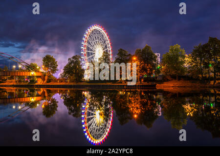 Germania, illuminate ruota panoramica Ferris e luci del gigante fiera sveva chiamato Cannstatter Wasen in Stuttgart City di notte riflettendo in neckar r Foto Stock