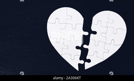 Puzzle di cuore diviso a metà, il giorno di san valentino, due piece jigsaw amore cuore puzzle, amore concetto. Puzzle cuore nero su sfondo di legno. A forma di cuore j Foto Stock