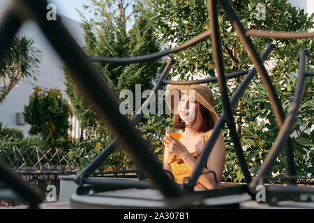 Ritratto di giovane ragazza asiatica seduta e di bere il succo d'arancia nel parco. Foto Stock