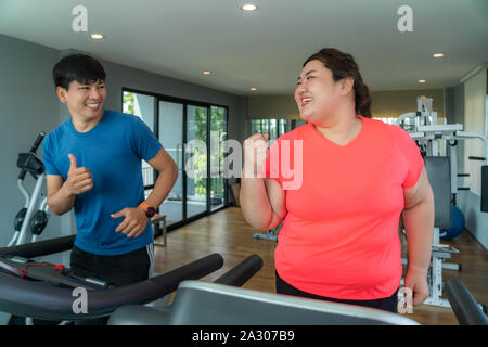 Due Asian trainer uomo e donna sovrappeso esercizio di formazione sul tapis roulant in palestra, trainer thump fino a lei per il buon risultato durante gli allenamenti. Donne grasse Foto Stock