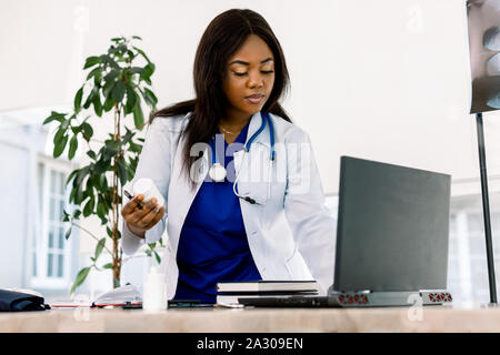 Femmina nero di medico del lavoro in un ufficio, cercando di laptop. Bella americano africano donna medico o infermiere lavorando su un computer portatile in moderno Foto Stock