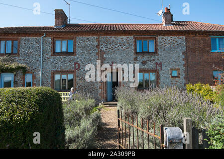 Capelli grigi nonna seduta su una panchina leggendo una rivista al di fuori della Hall Wiveton holiday cottages in Marsh Lane, Wiveton, North Norfolk, Regno Unito Foto Stock