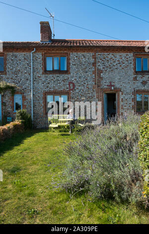 Capelli grigi nonna seduta su una panchina leggendo una rivista al di fuori della Hall Wiveton holiday cottages in Marsh Lane, Wiveton, North Norfolk, Regno Unito Foto Stock