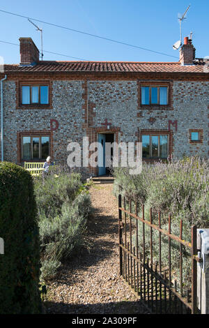 Capelli grigi nonna seduta su una panchina leggendo una rivista al di fuori della Hall Wiveton holiday cottages in Marsh Lane, Wiveton, North Norfolk, Regno Unito Foto Stock