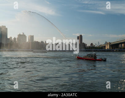 New York City - Circa 2019: FDNY vigili del fuoco in barca la spruzzatura di acqua in tubo in aria per celebrare e onorare il passaggio della flotta della marina militare entrando in porto di new york Foto Stock