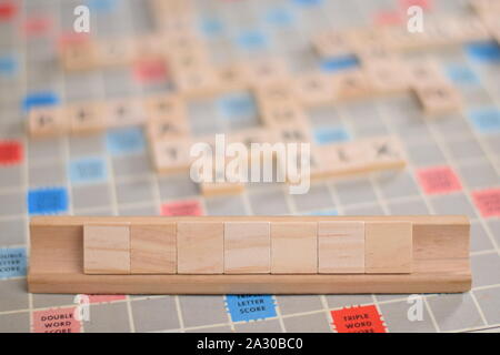 7 vuoto in legno piastrelle scrabble su una piastrella-rack, per voi per riempire la propria parola. Sullo sfondo di una scheda vintage, fuori fuoco con spazio di copia Foto Stock