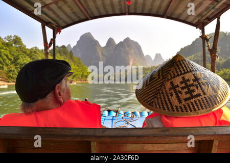 Senior turista giovane godetevi il fiume Li splendidi e verdi picchi di montagna da zattera di bambù in barca, nel Guangxi, Cina Foto Stock