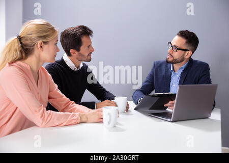 Felice Coppia Giovane consultazione amichevole maschio Advisor finanziario con tazze da caffè alla scrivania in ufficio Foto Stock