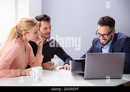 Felice Coppia Giovane consultazione amichevole maschio Advisor finanziario con tazze da caffè alla scrivania in ufficio Foto Stock